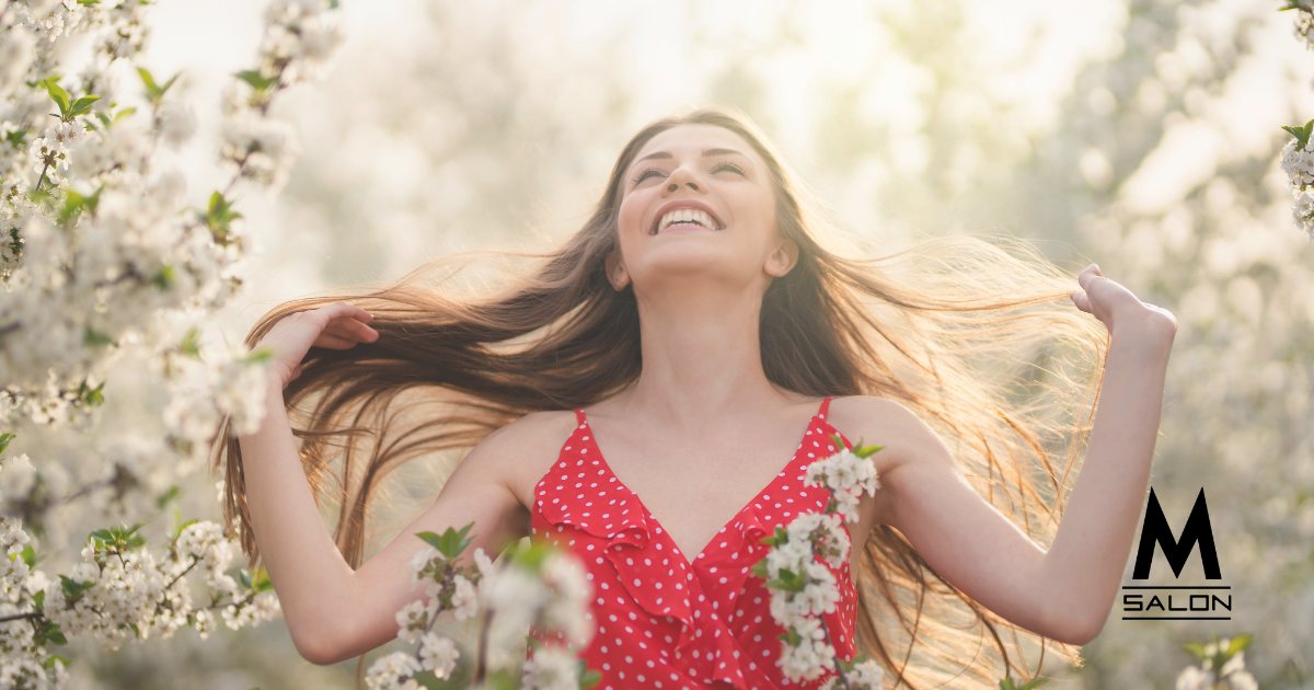 A woman in a red dress is standing in front of a cherry blossom tree.