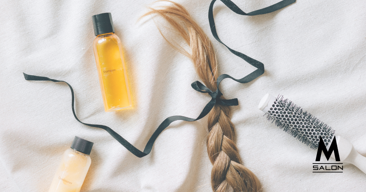 A braided hair is sitting on a white towel next to bottles of shampoo and a brush.