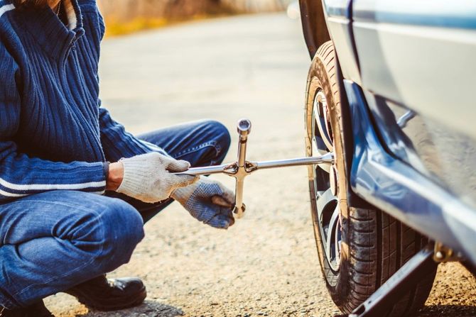 Person changing a tire on the side of the road, using a lug wrench.