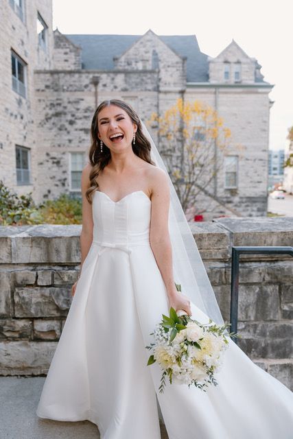 A bride in a white dress is holding a bouquet of purple and pink flowers.