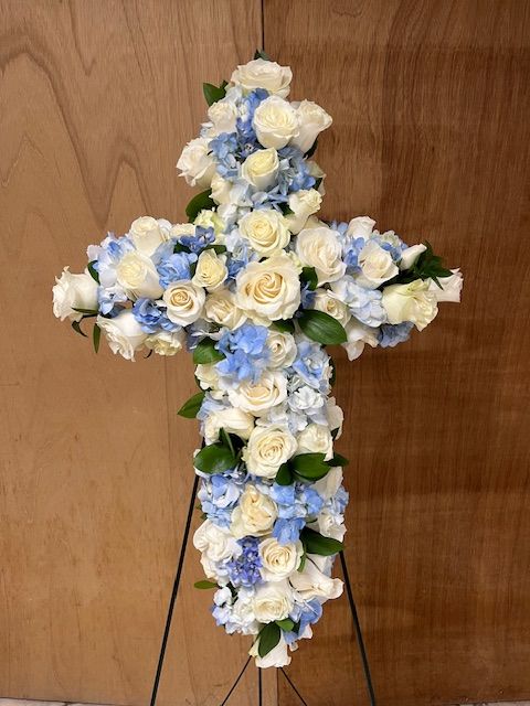 A cross made of white and blue flowers is sitting on a wooden table.