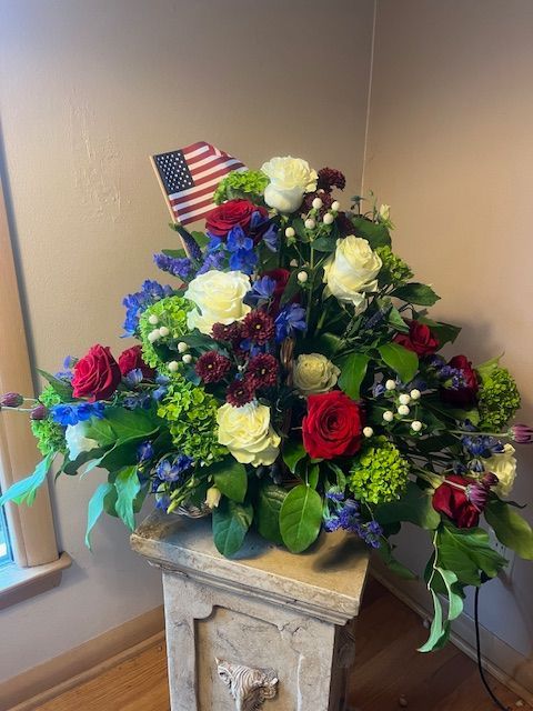 A vase filled with red , white and blue flowers with an american flag on top.