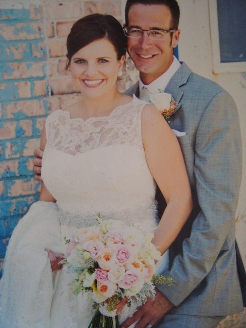 A bride and groom pose for a picture in front of a brick wall