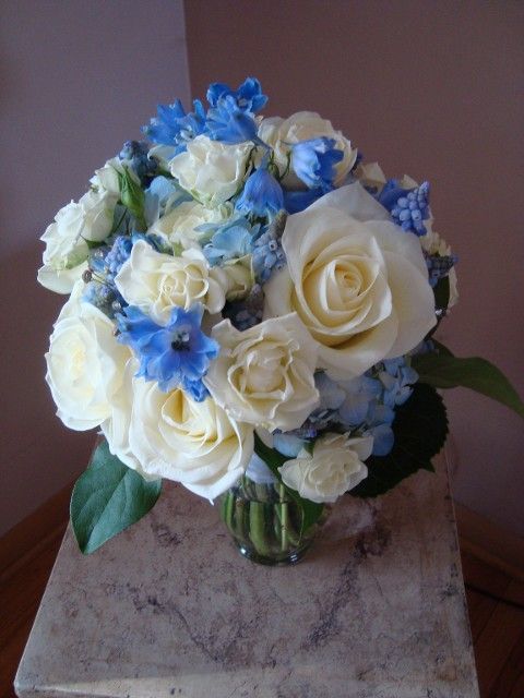 A vase filled with white roses and blue flowers