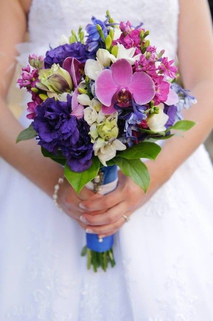 A woman in a white dress is holding a bouquet of purple and white flowers