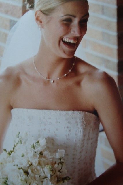 A woman in a wedding dress is smiling and holding a bouquet of white flowers