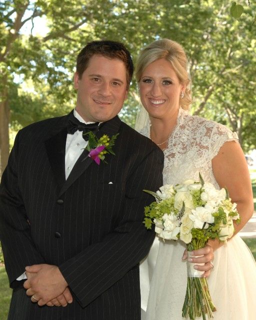 A bride and groom are posing for a picture and the bride is holding a bouquet of flowers