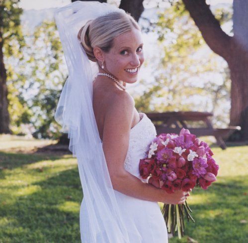 A bride in a white dress is holding a bouquet of pink and white flowers
