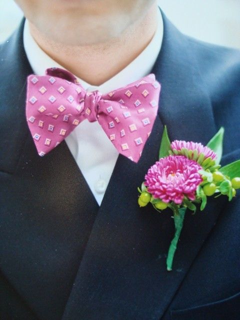 A man in a suit has a pink bow tie and a pink flower in his pocket