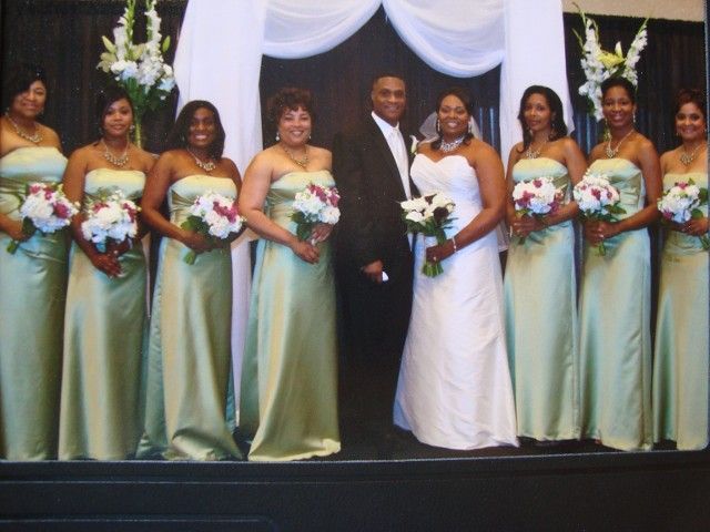 A bride and groom pose with their bridesmaids in green dresses