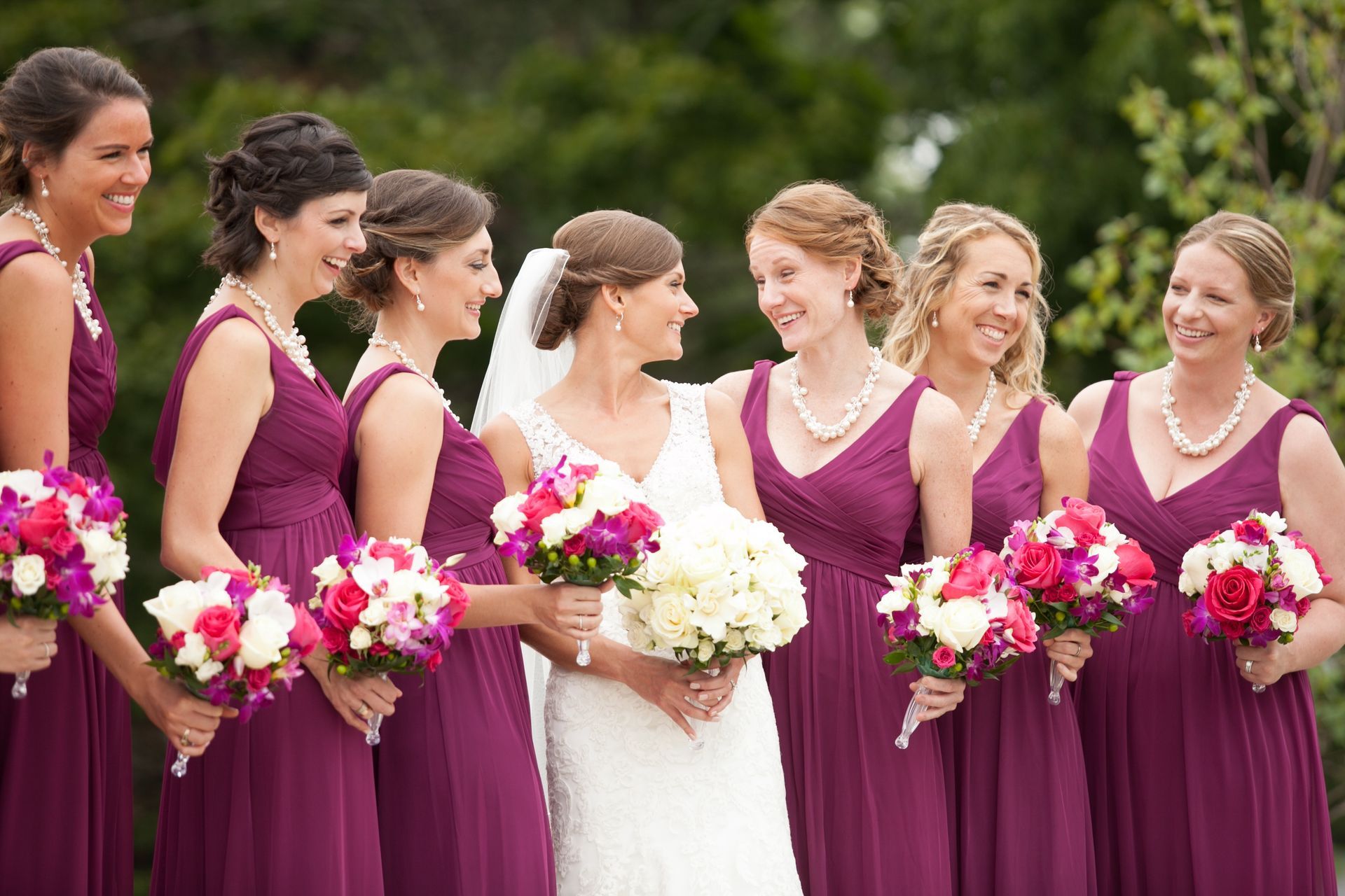 The bride and her bridesmaids are wearing purple dresses and holding bouquets of flowers.