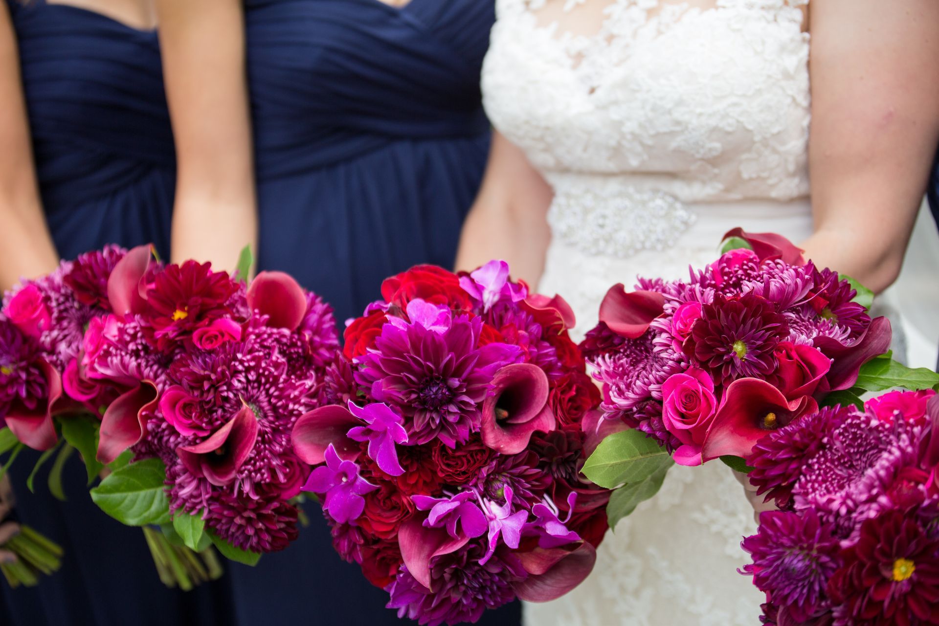A bride and her bridesmaids are holding bouquets of purple and red flowers