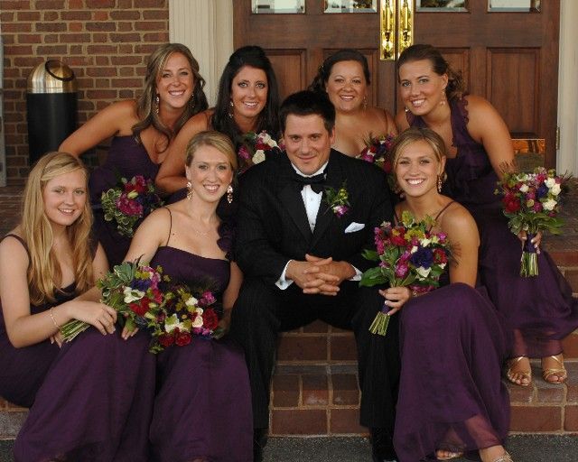 A bride and groom pose with their bridesmaids in purple dresses