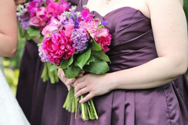 A woman in a purple dress is holding a bouquet of pink and purple flowers.