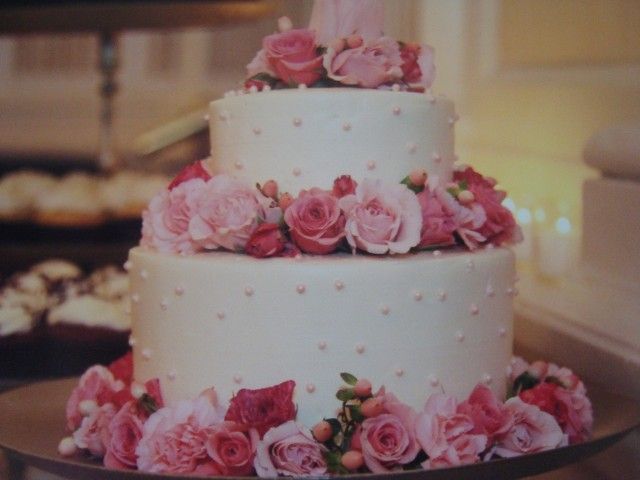 A wedding cake with pink roses and pearls on it