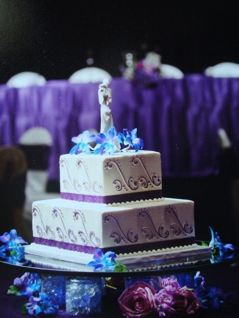A purple and white wedding cake with a bride and groom on top