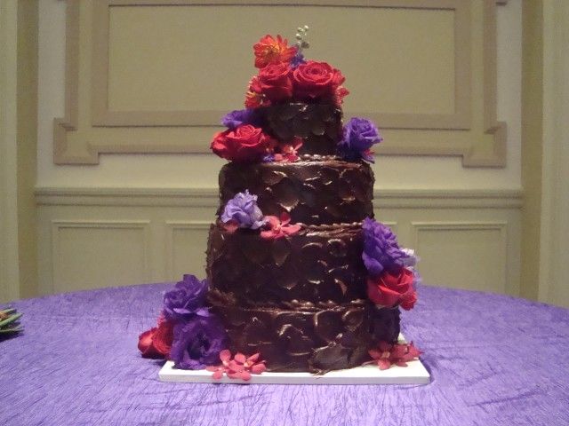 A chocolate cake with purple and red flowers on top