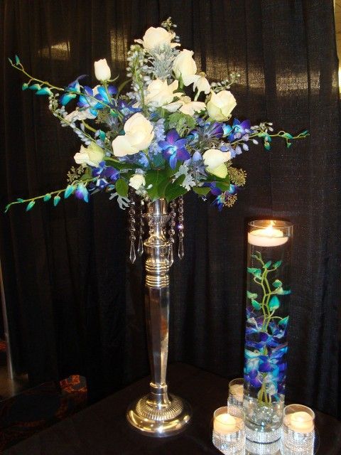 A silver vase filled with blue and white flowers sits on a table next to candles