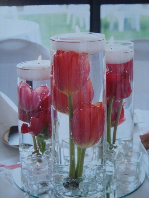 Three vases filled with red flowers and candles on a table