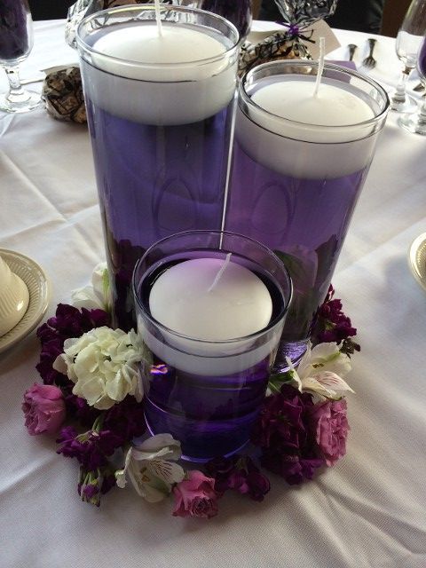 Three purple vases with floating candles and flowers on a table