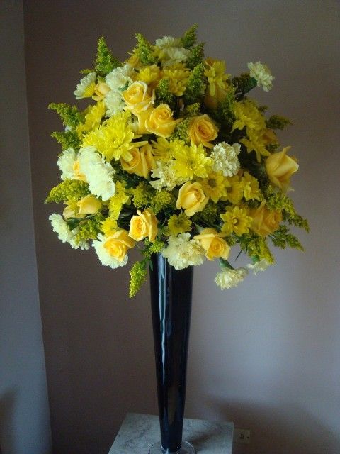 A tall black vase filled with yellow and white flowers