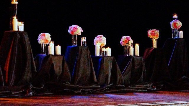 A row of tables with candles and flowers on them on a stage.