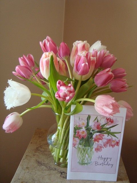 A vase of pink and white tulips next to a happy birthday card