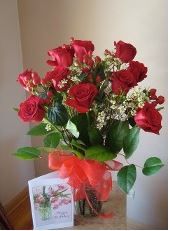 A vase filled with red roses and a card on a table.