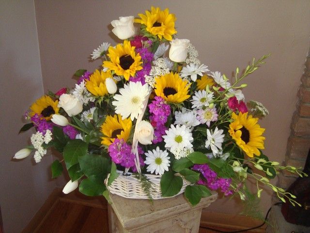 A basket filled with flowers including sunflowers and daisies