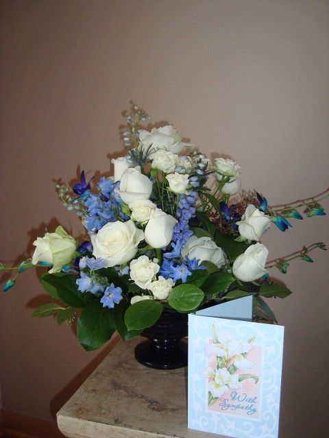 A vase filled with white roses and blue flowers next to a birthday card