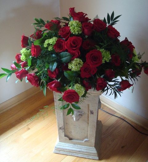 A vase filled with red roses and green flowers