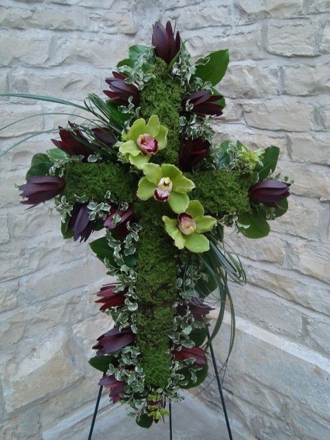 A cross made of moss and flowers against a stone wall