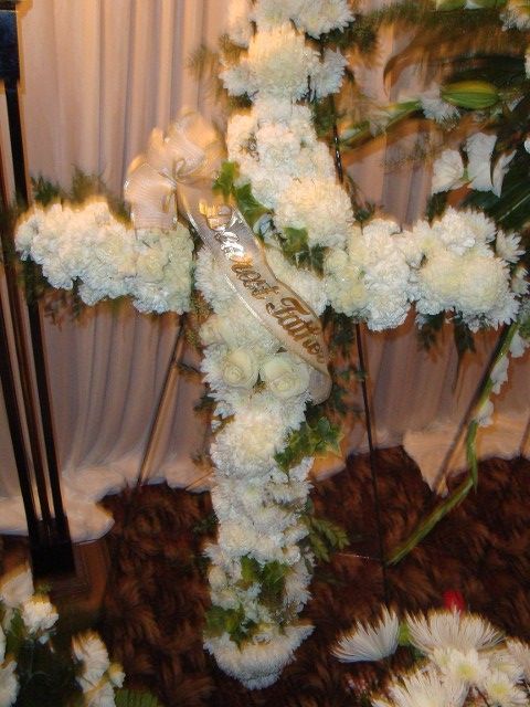 A cross made of white flowers with a ribbon that says