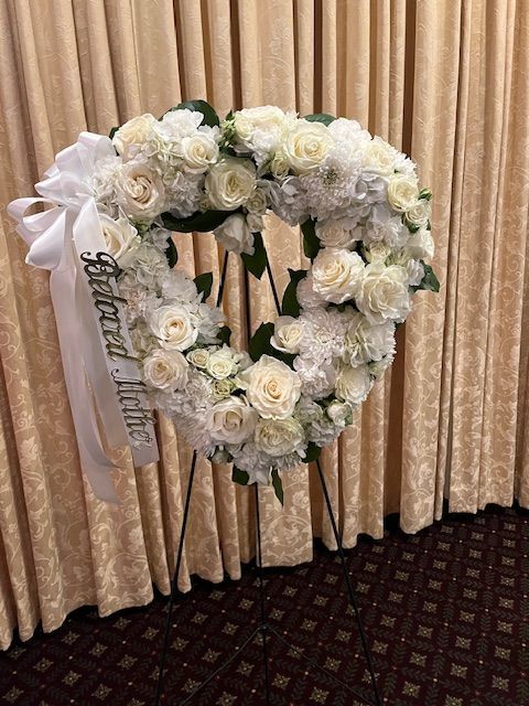 A heart shaped wreath made of white flowers is sitting in front of a curtain.