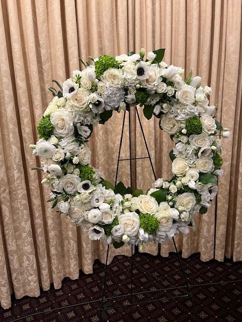A wreath of white flowers is sitting on a stand in front of a curtain.