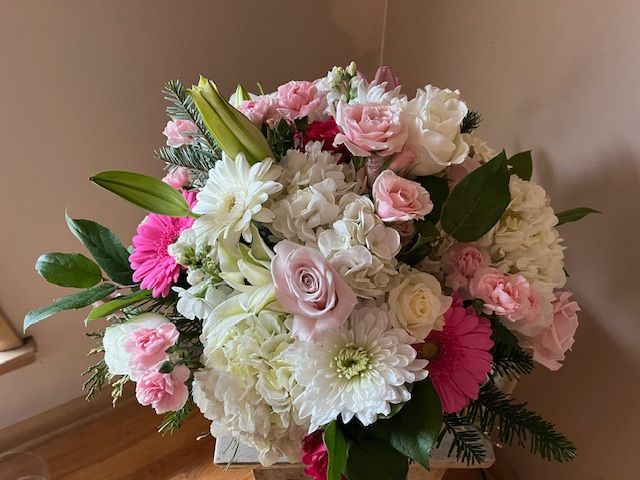 A vase filled with pink and white flowers is sitting on a wooden table.