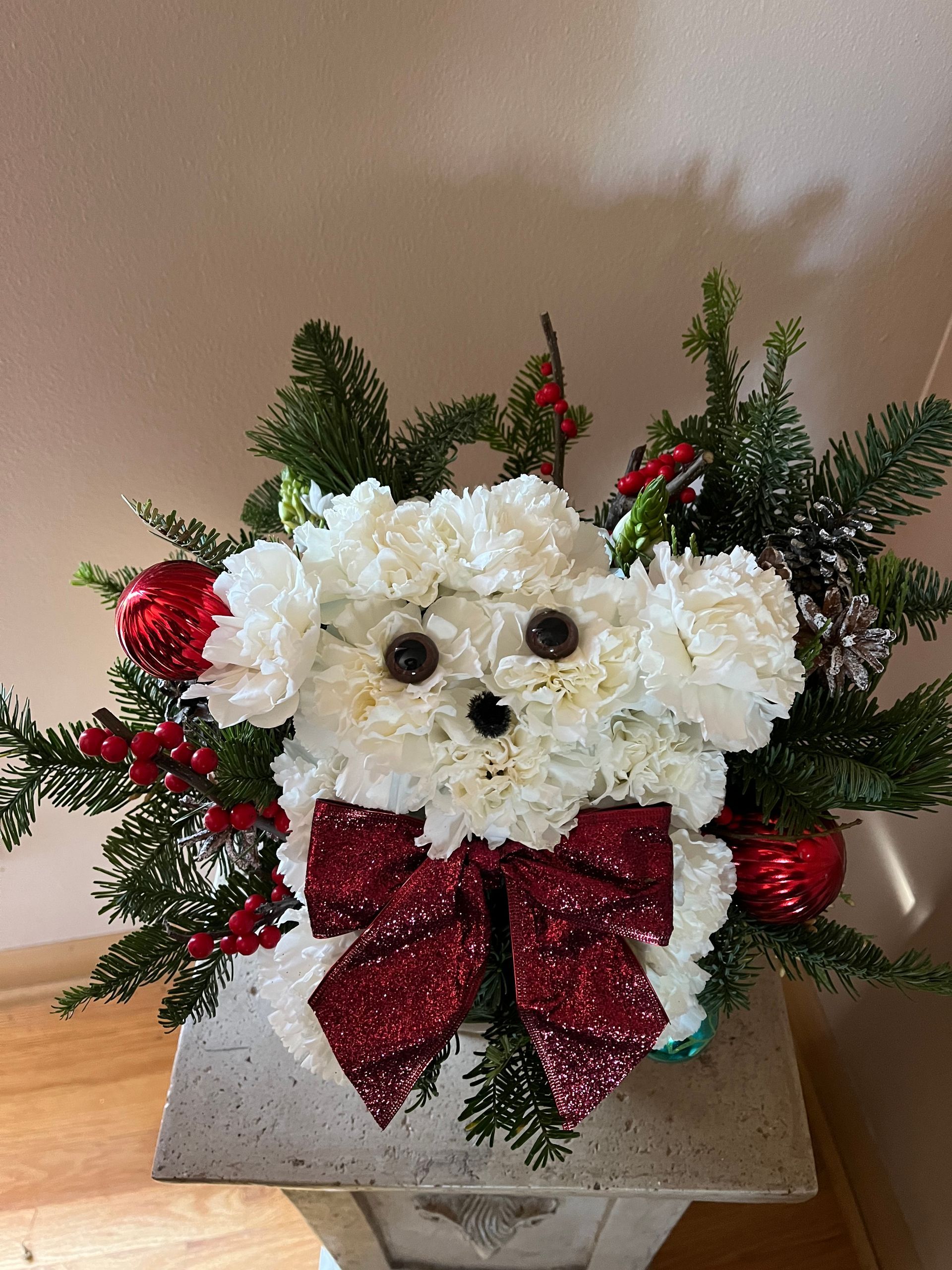 A white teddy bear made out of flowers with a red bow.