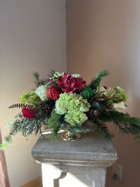 A vase filled with flowers and pine cones is sitting on a pedestal.