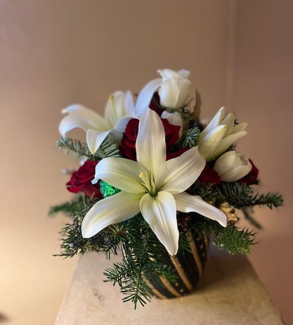 A vase filled with white lilies and red roses is sitting on a table.