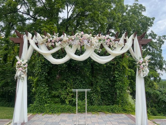 A wedding arch is decorated with flowers and white cloth.