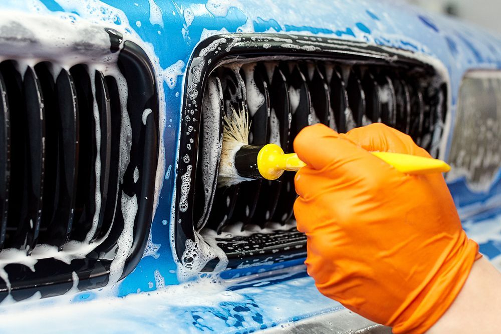 A Person is Cleaning the Grill of a Car With a Brush — Detail World Car Detailing in Coffs Harbour, NSW