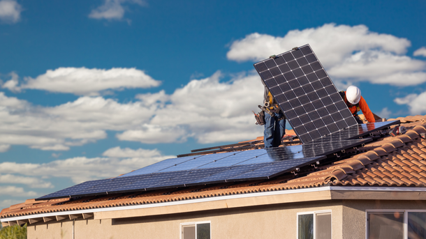 A man is installing solar panels on the roof of a house.