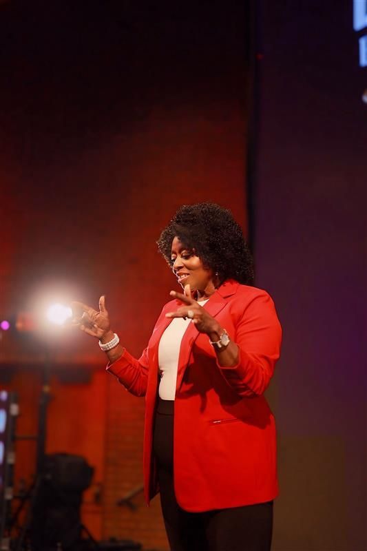 A woman wearing a black shirt and a red lei is smiling while sitting at a table.