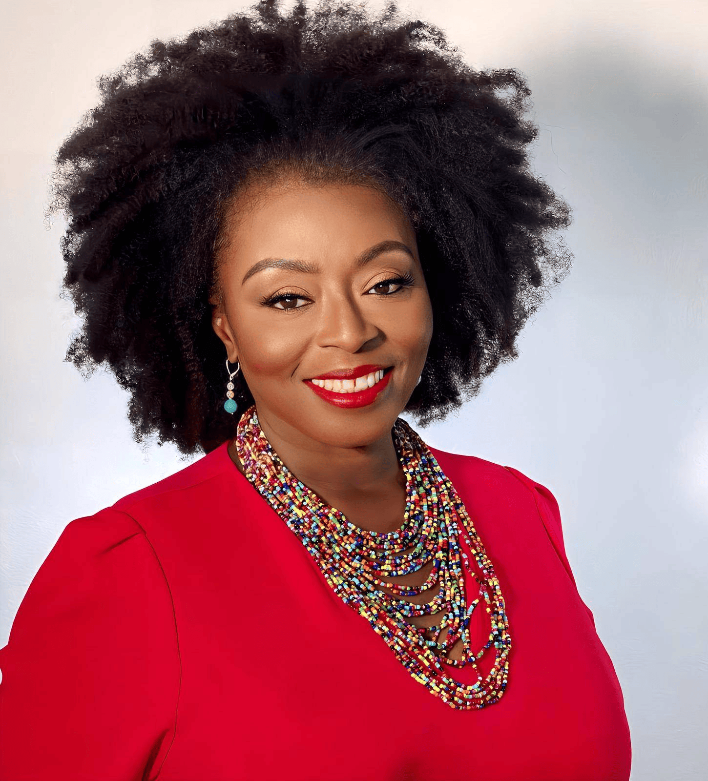 A woman wearing a red shirt and a colorful necklace smiles for the camera.