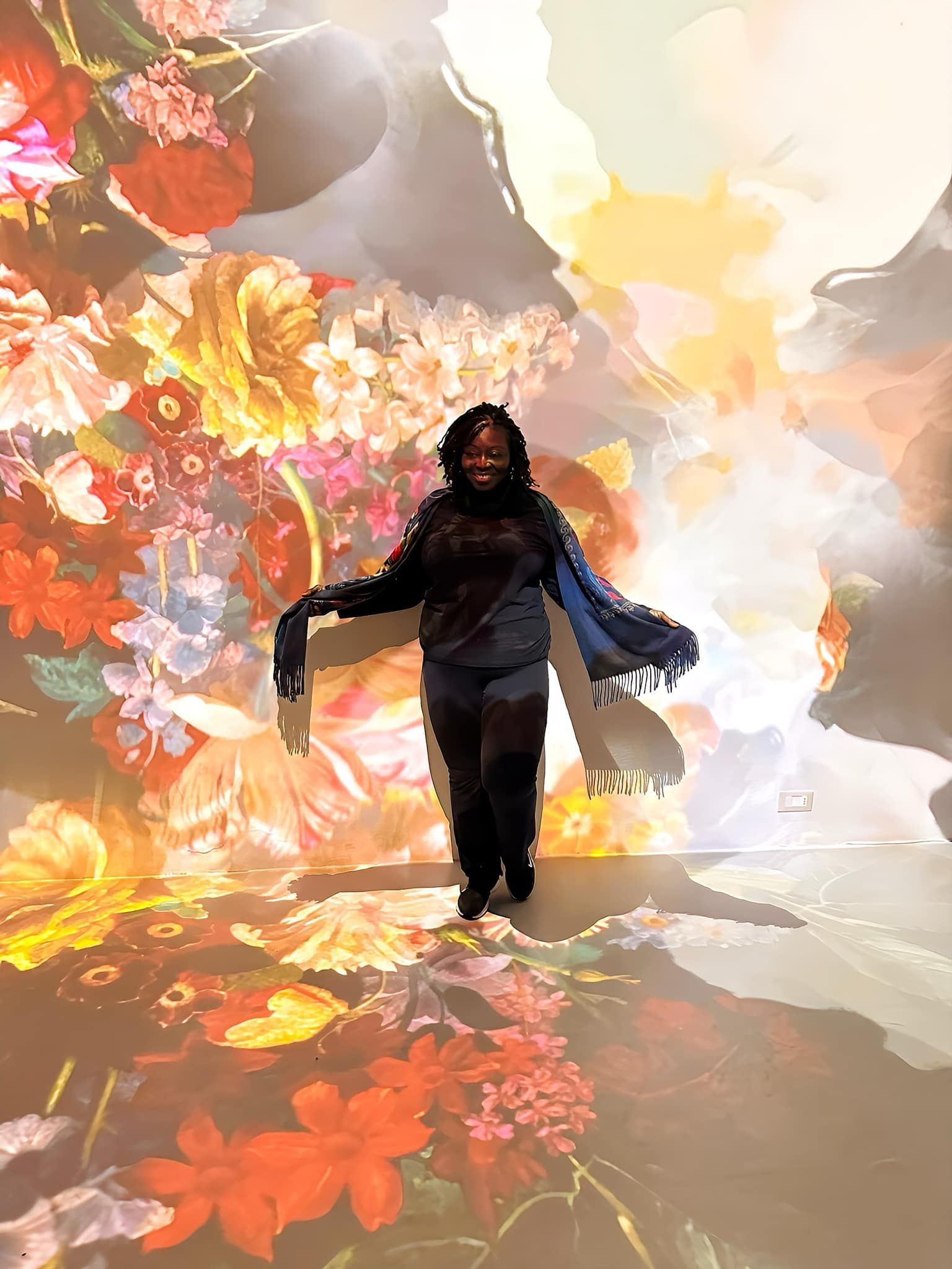 A woman is standing in front of a painting of flowers.