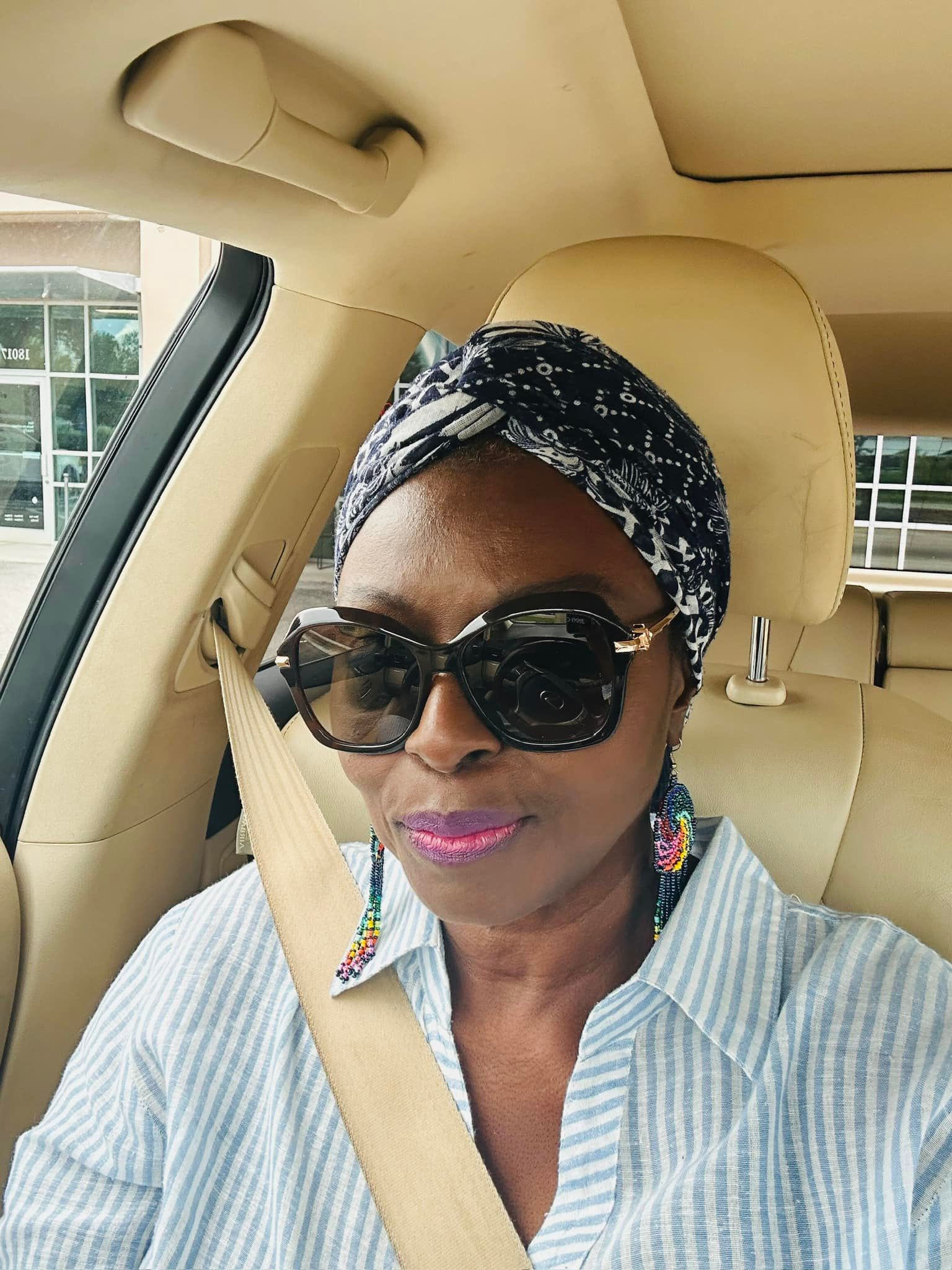 A woman wearing sunglasses and a head scarf is sitting in a car.