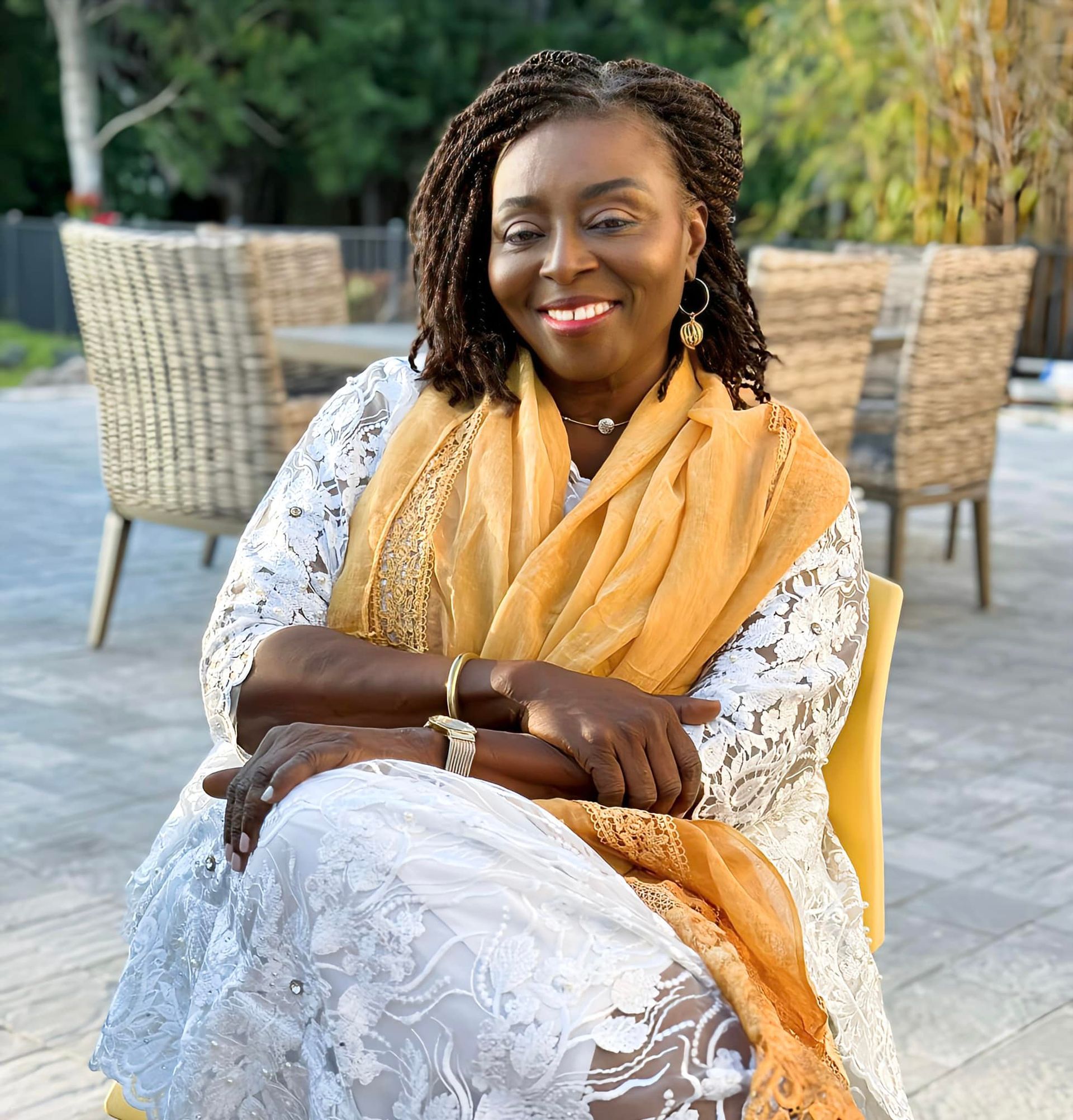 A woman wearing a white dress and a yellow scarf is sitting in a chair.