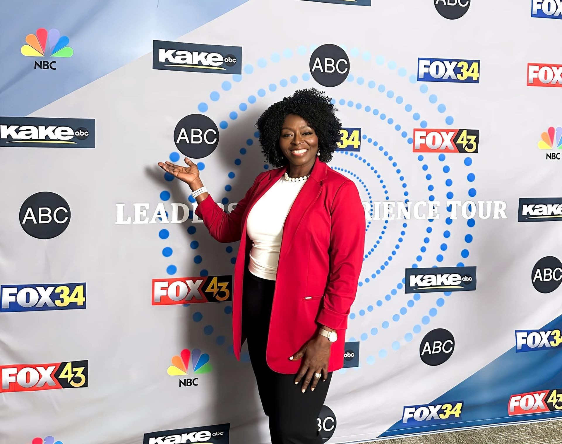 A woman in a red jacket is standing in front of a wall with logos on it.