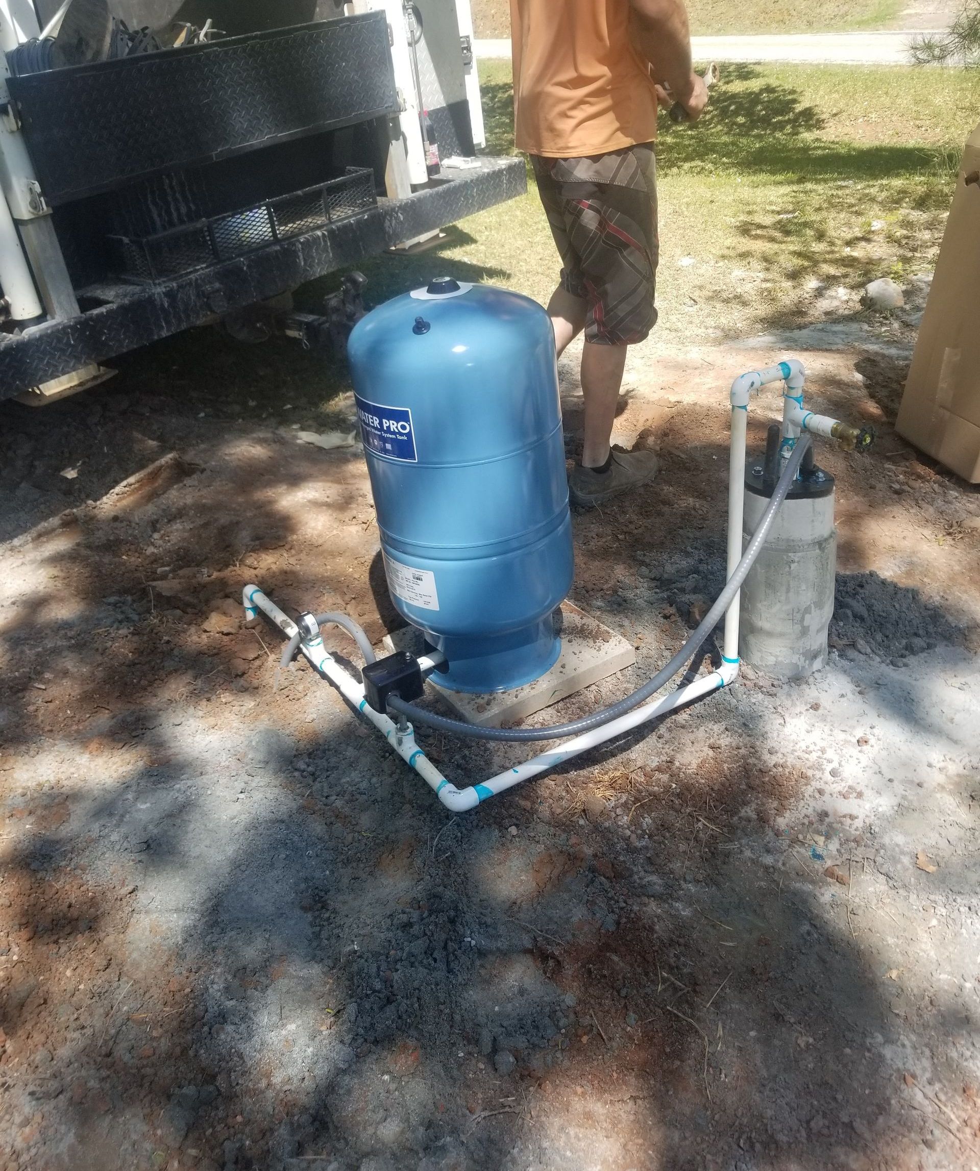 Blue water pressure tank and well, connected by white pipes, with person in background.