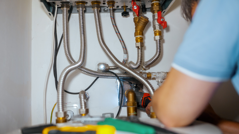 Person working on pipes connected to a boiler, using a wrench.